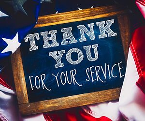 Chalkboard in picture frame with American flag behind it. The chalkboard reads "Thank you for your service"