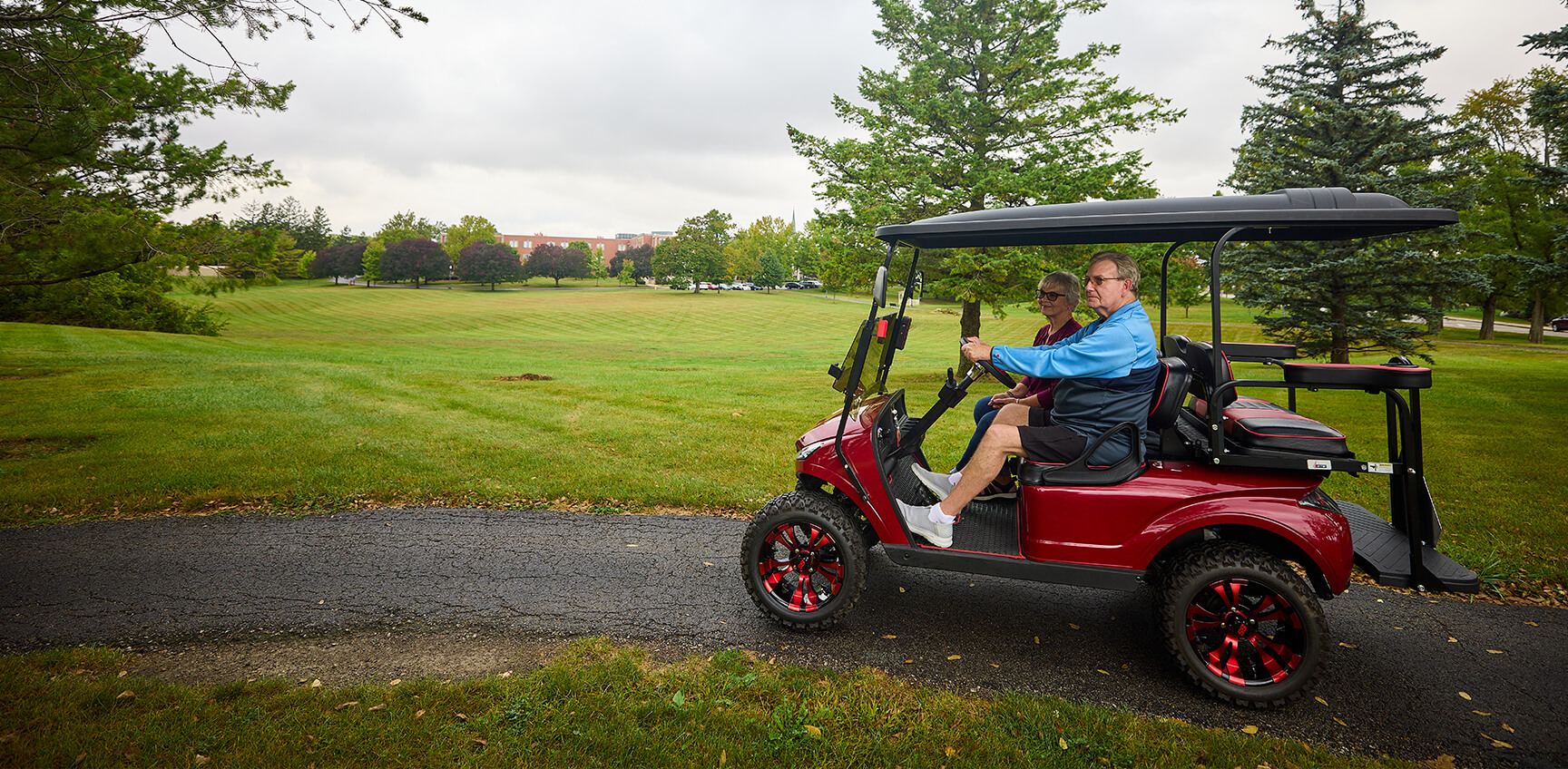 Two people driving golf cart on path