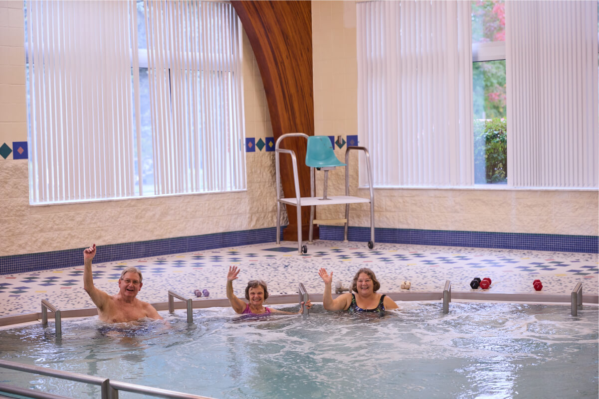 Three seniors waving from in the pool