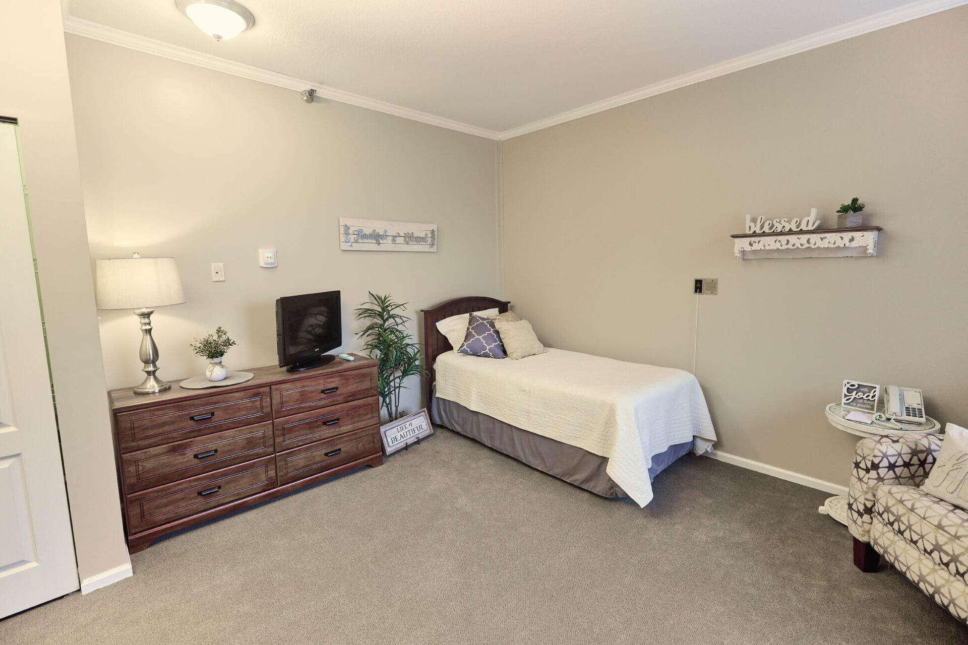Twin bed next to dresser with a TV facing a sitting area in room