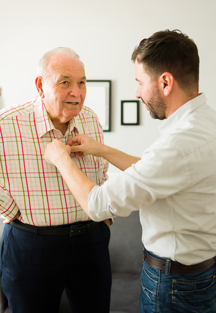 Employee assisting senior with buttoning his shirt