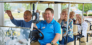 Seniors waving in golf cart driven by Heritage Point employee