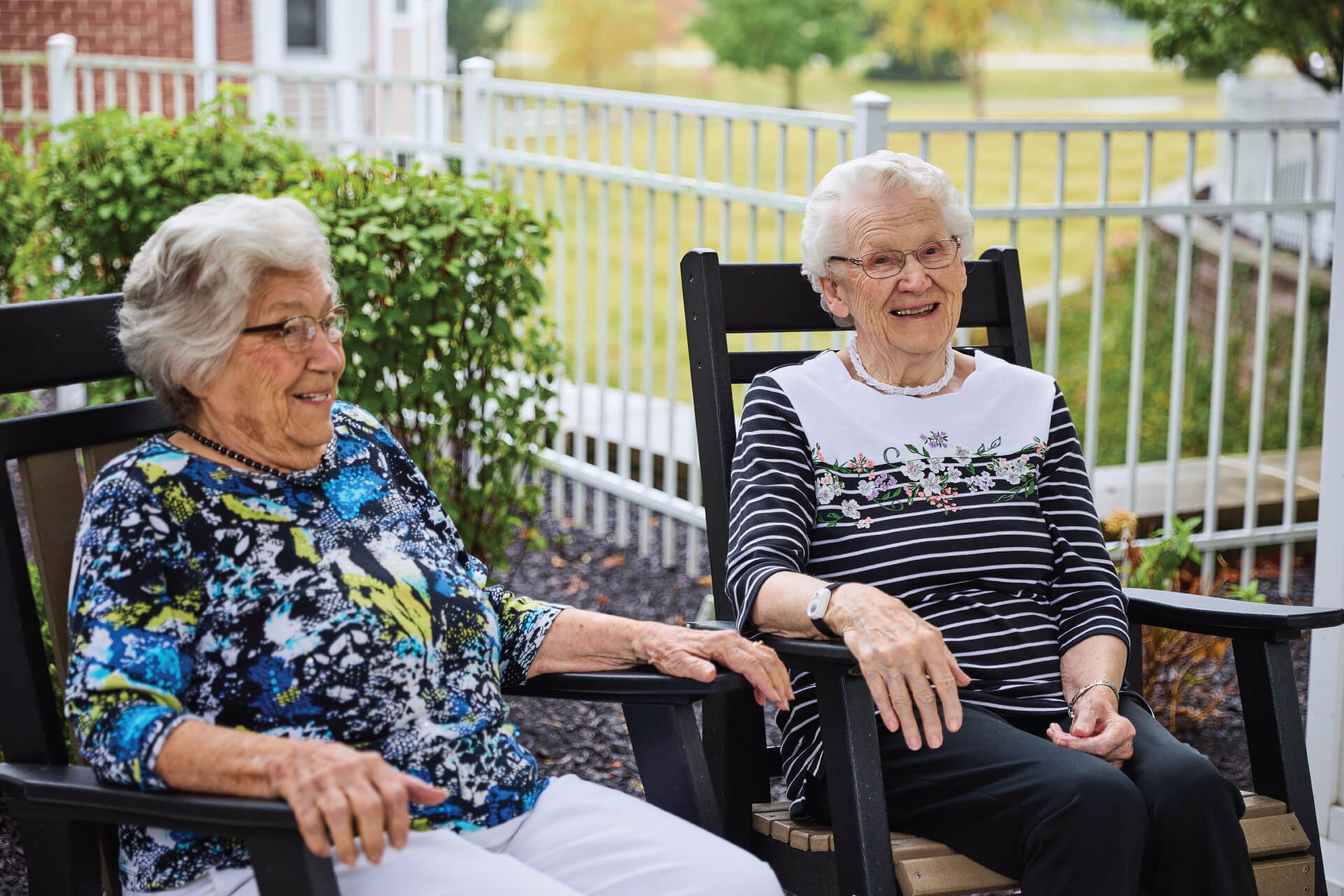 Two senior women laughing in outdoor rocking chairs