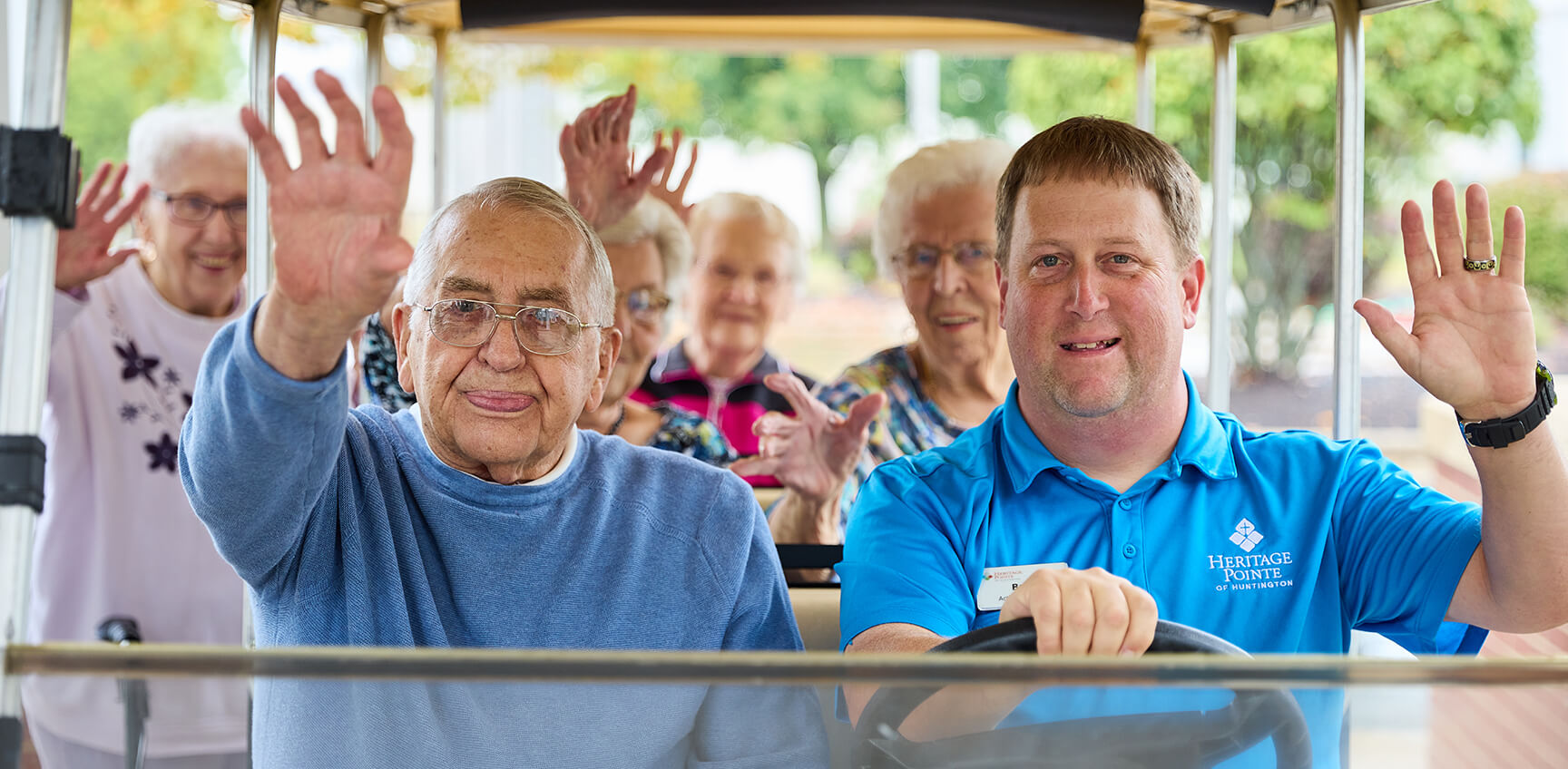 Seniors waving from a golf cart driven by heritage employee