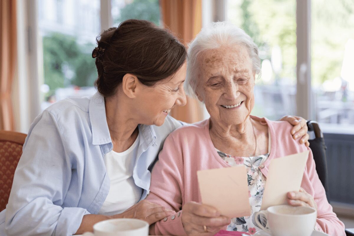 Senior woman and her caretaker smiling and looking at old photographs together.