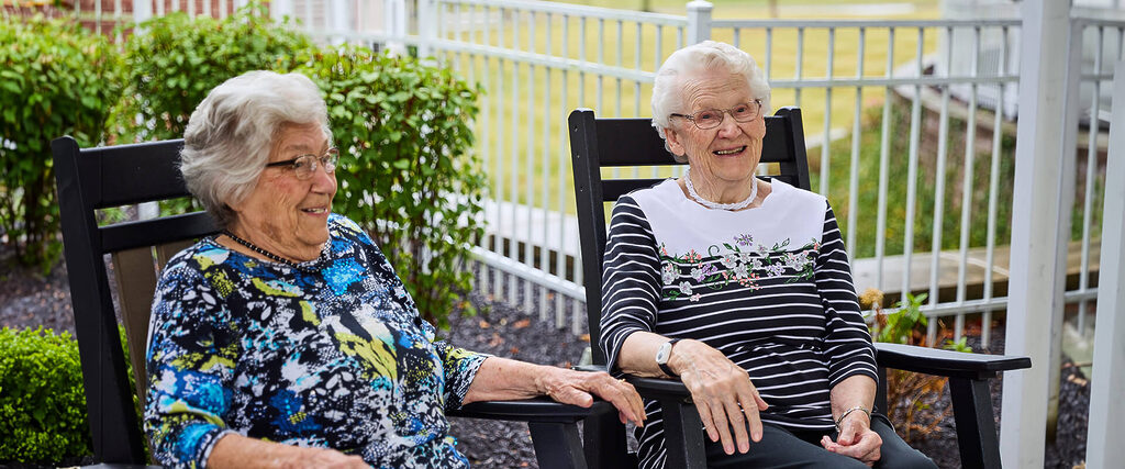 Two residents sit on rocking chairs outdoors