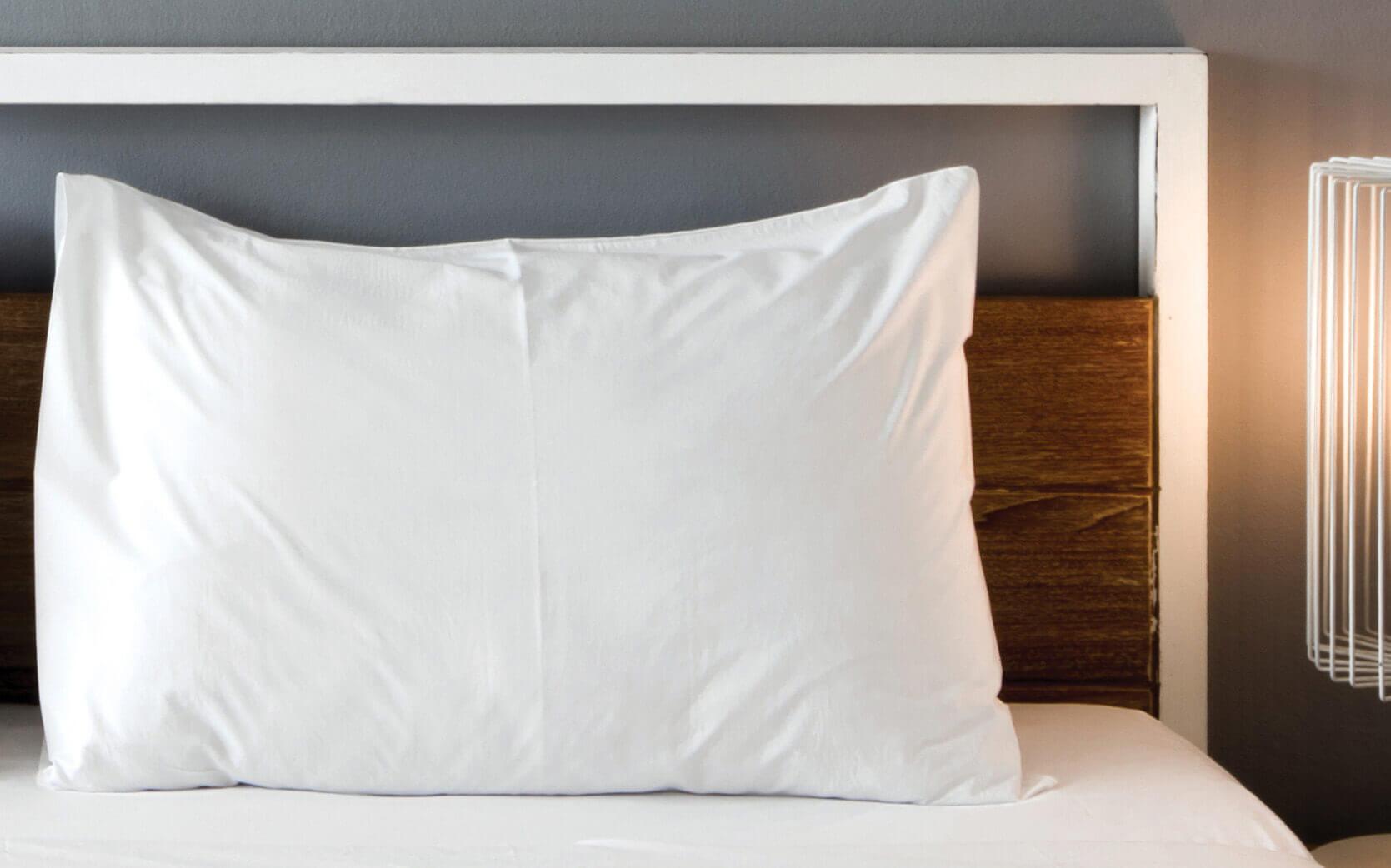 Cozy bed with white pillow and wooden headboard under soft lighting.