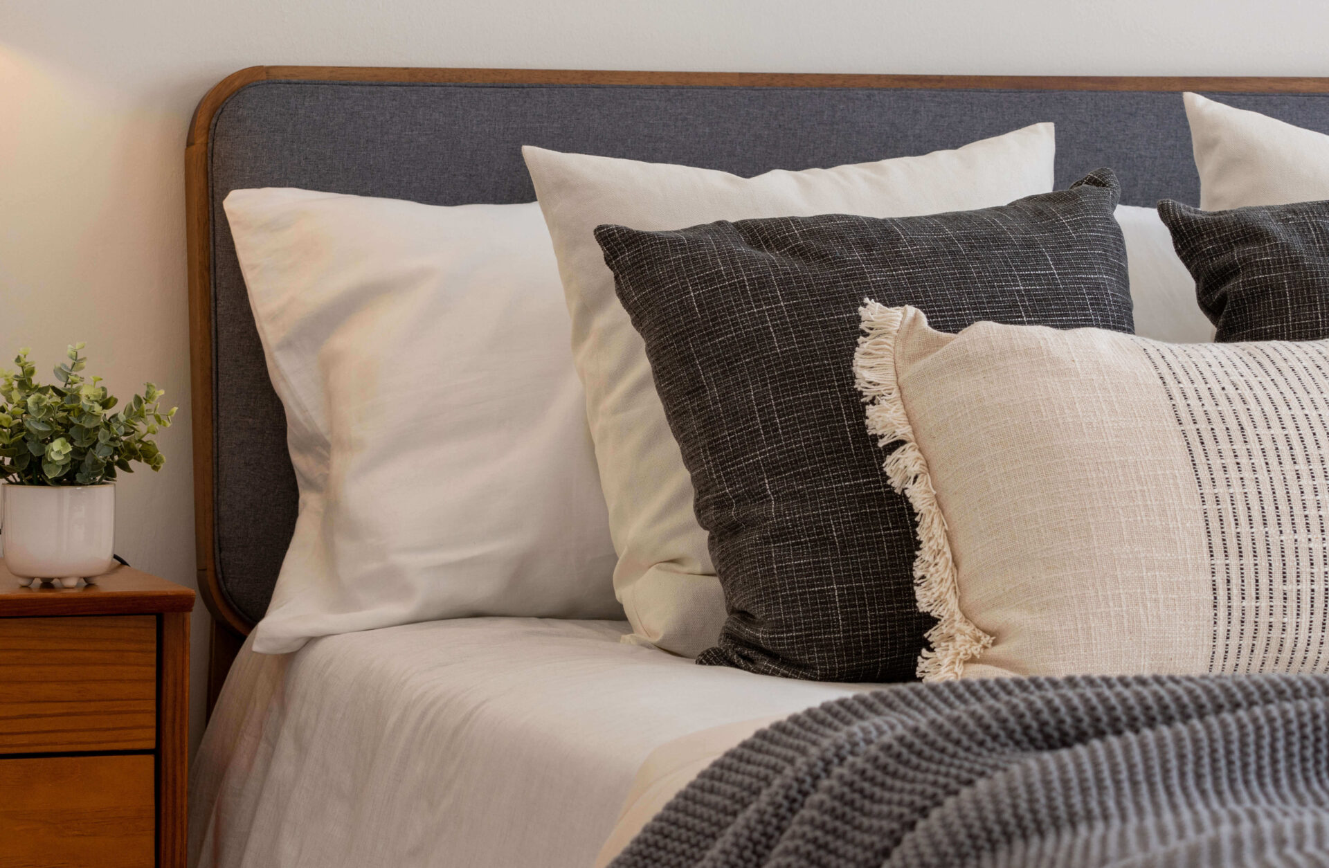 Comfortable bedding with decorative pillows and nightstand in cozy living unit.