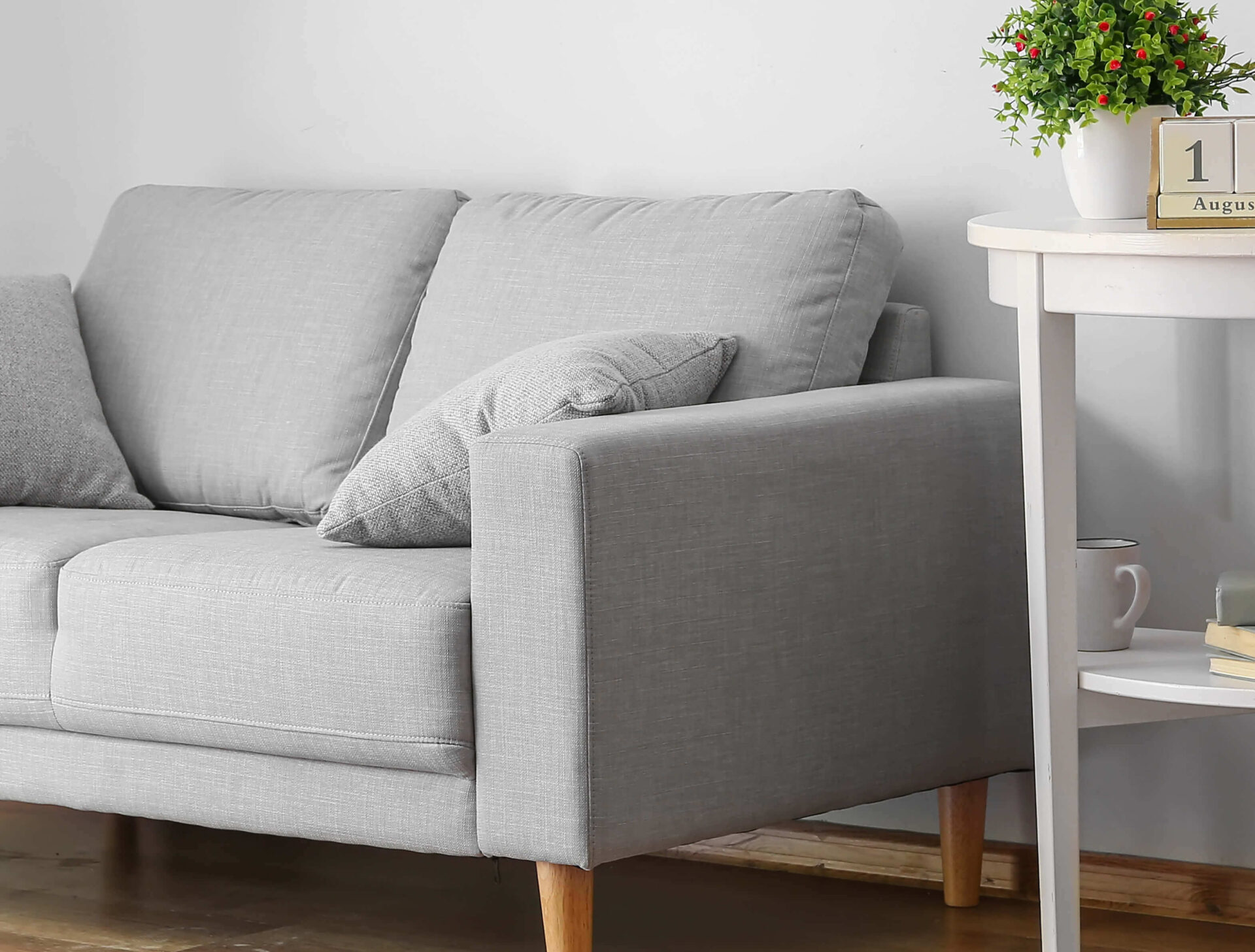 Cozy gray sofa with cushions next to a white round table with plant and calendar.