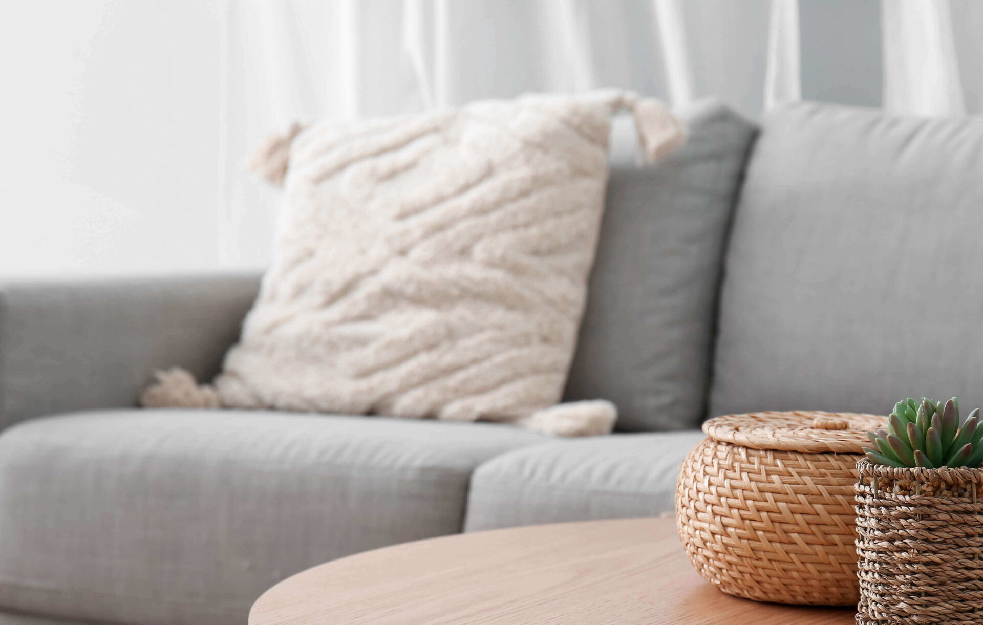 Cozy unit interior with gray couch, fluffy pillow, and woven decor on table.