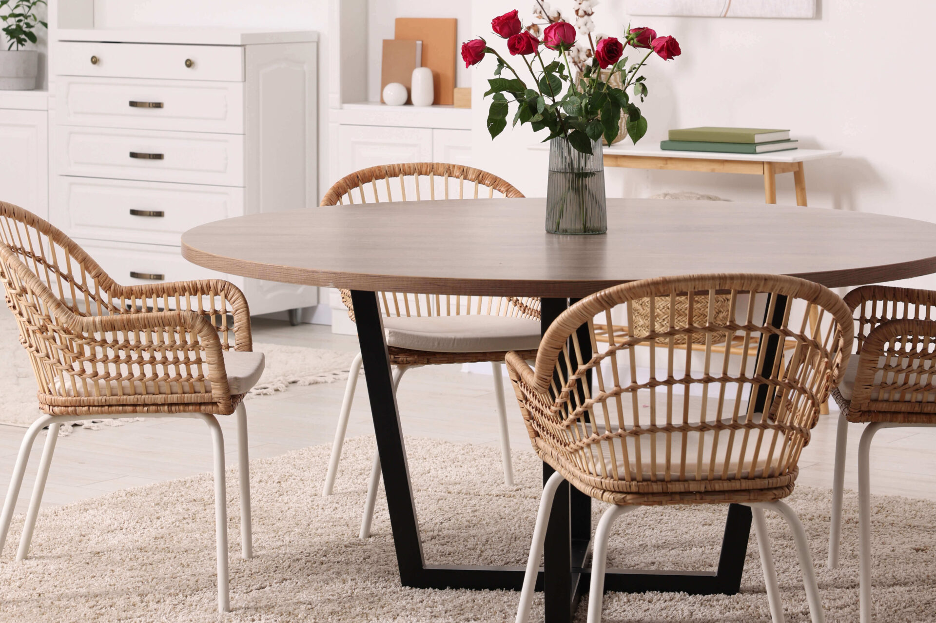 Round table with wicker chairs and vase of red roses in a bright living space.