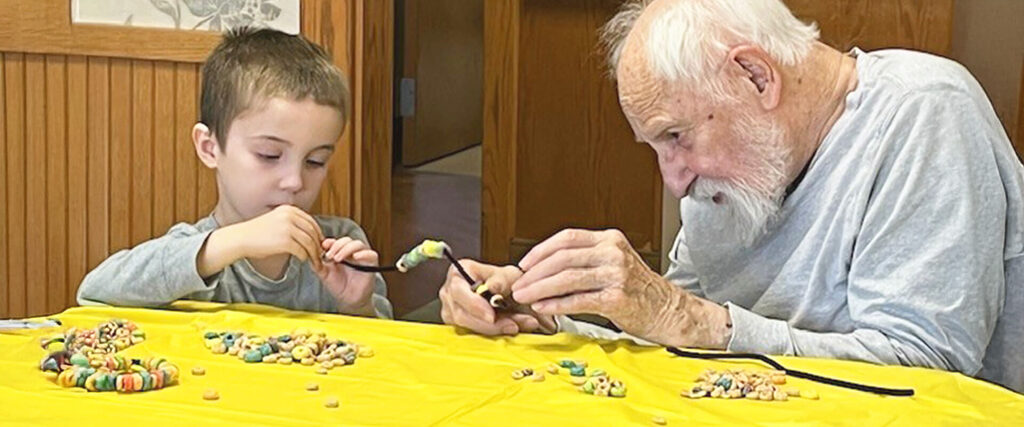 Senior man and young grandchild do a craft on a yellow table