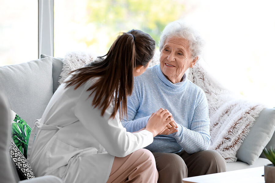 Caregiver warmly talks to an elderly woman in a cozy living room setting.