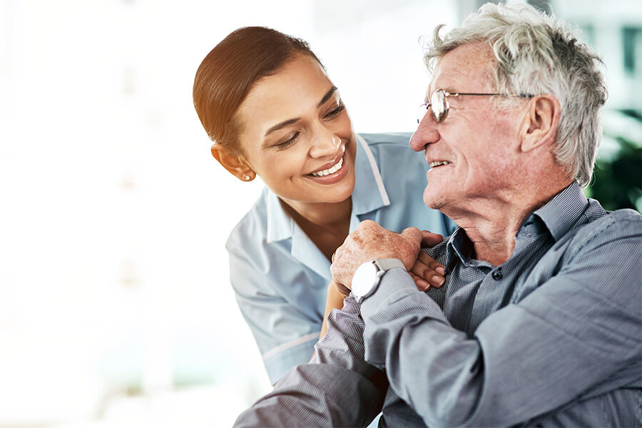 Smiling caregiver supports elderly man in a senior living unit.