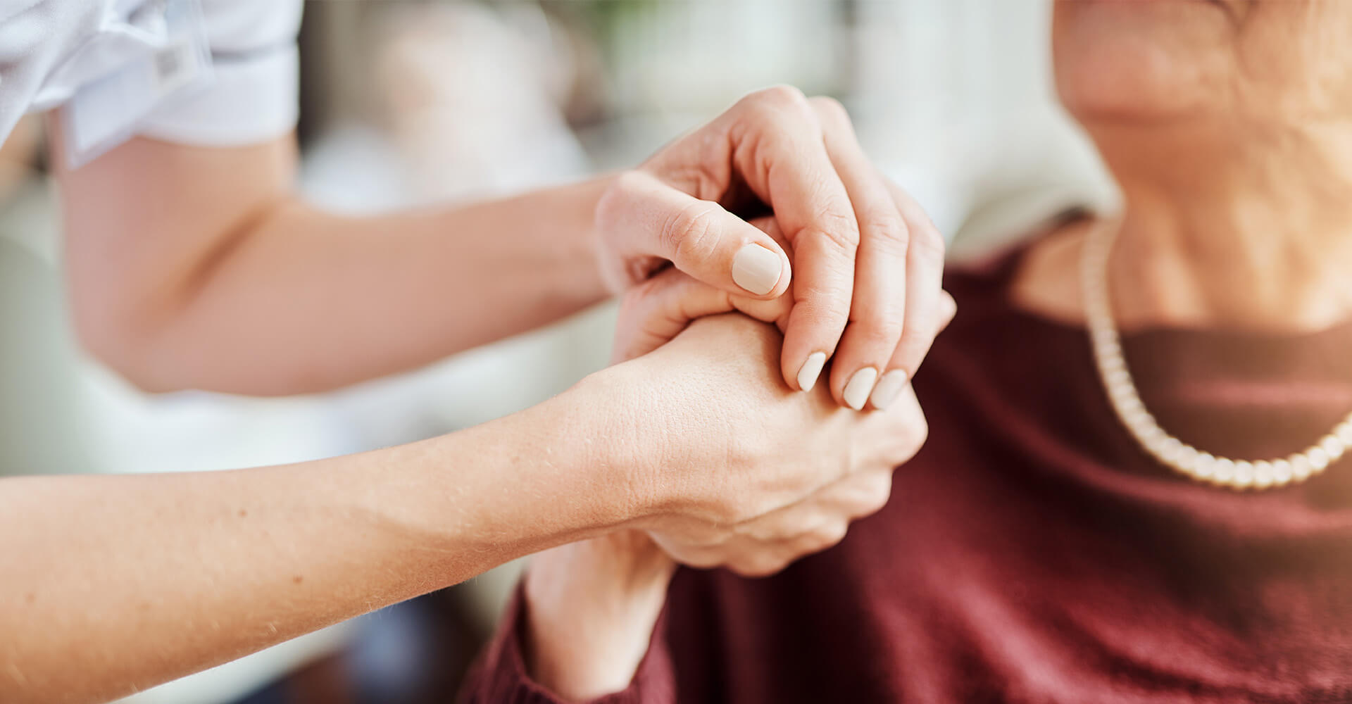 Caregiver gently holding older womans hands in comforting manner.
