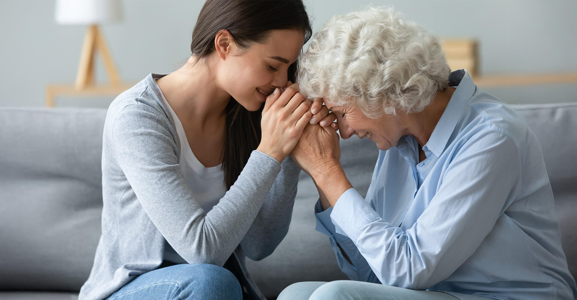Young and elderly women sharing a tender moment on a gray couch.