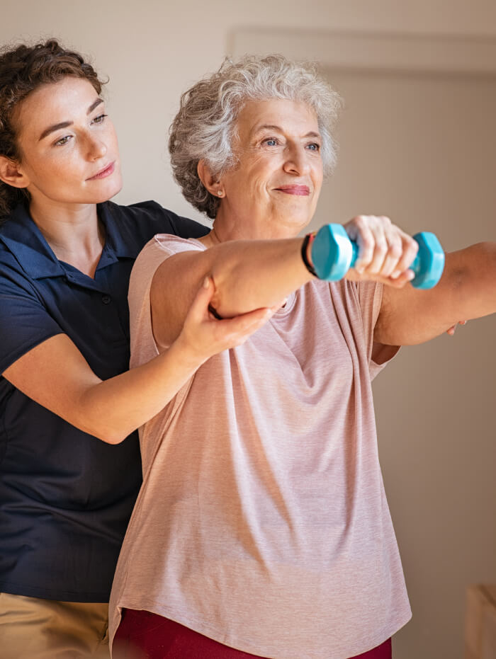 senior woman being guided to lift weights by a therapist
