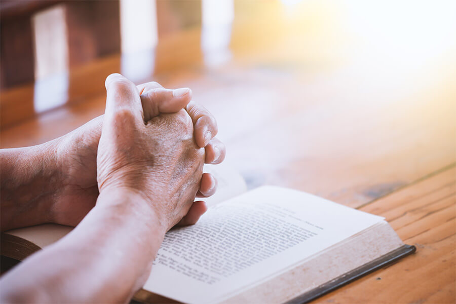 Hands of a person resting on an open book on a wooden table.