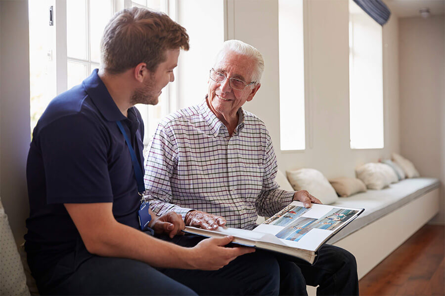 Young man and elderly man sharing a photo album in a bright living area.