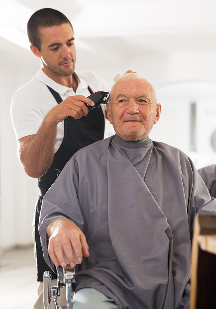 Barber trims hair of senior man in a community facility barbershop.