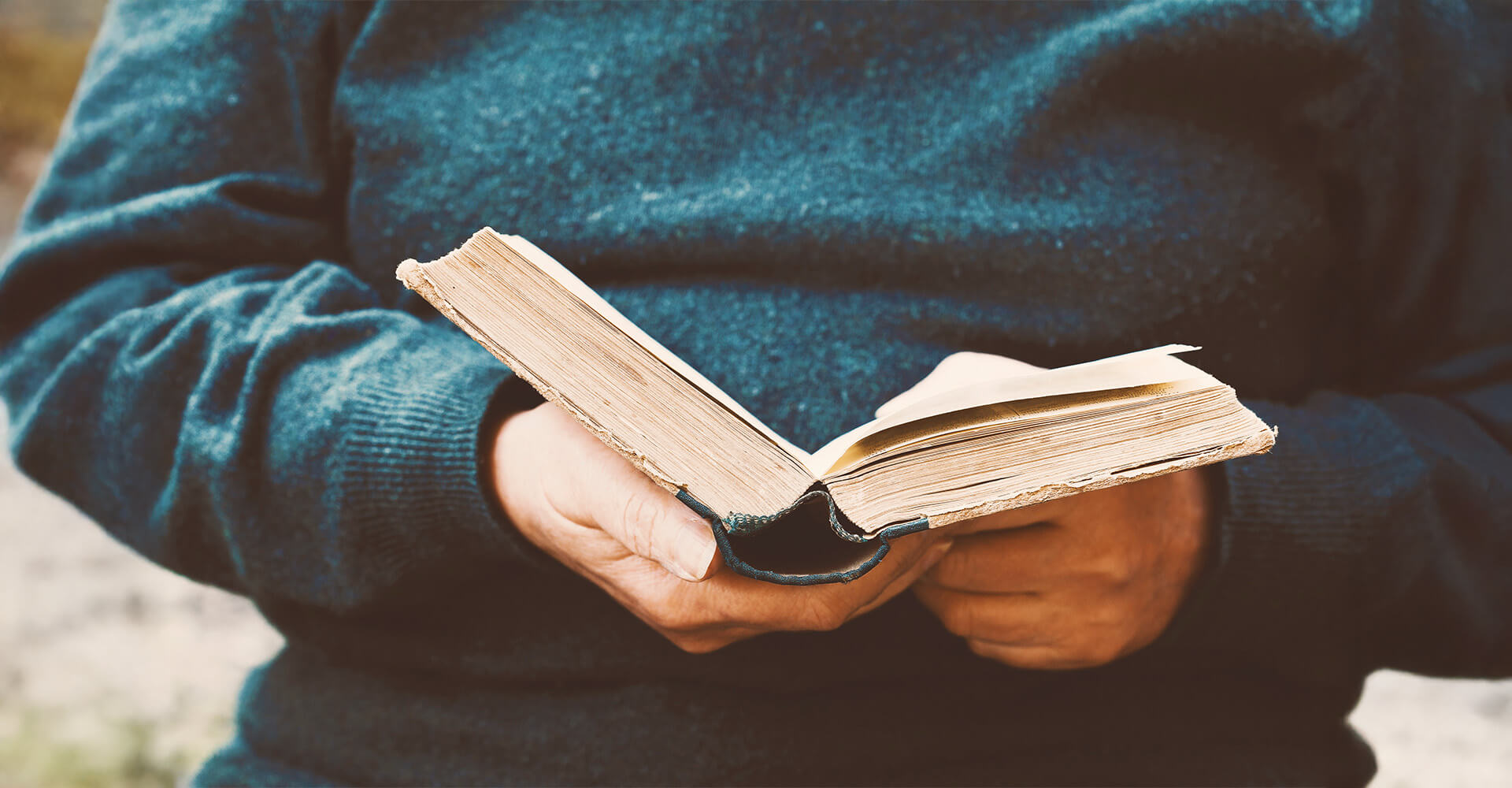 Person wearing a blue sweater holding and reading an open book.