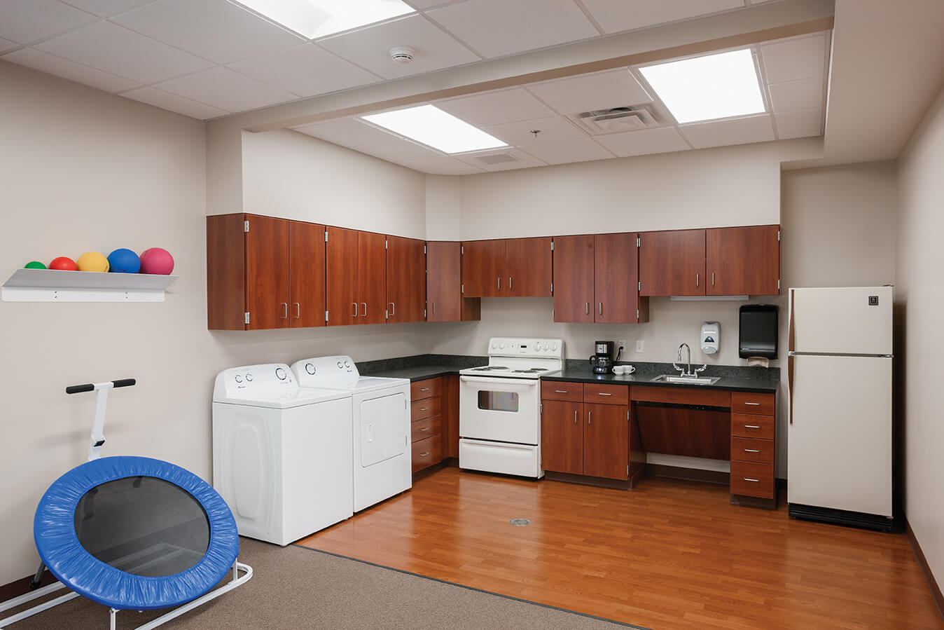 Unit kitchen with wooden cabinets, washer, dryer, and exercise equipment.