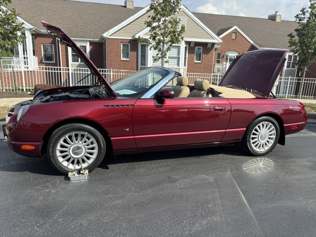 Red convertible with open hood and trunk parked in front of brick living units.