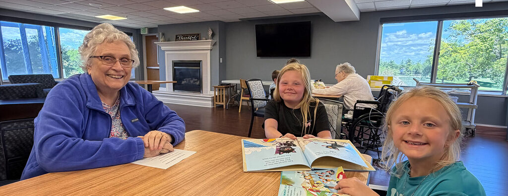 two young girls and senior woman around a table reading together