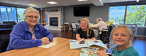 two young girls and senior woman around a table reading together