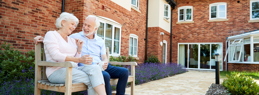 Senior couple laughing on bench in courtyard