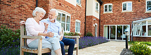 Senior couple laughing on bench in courtyard