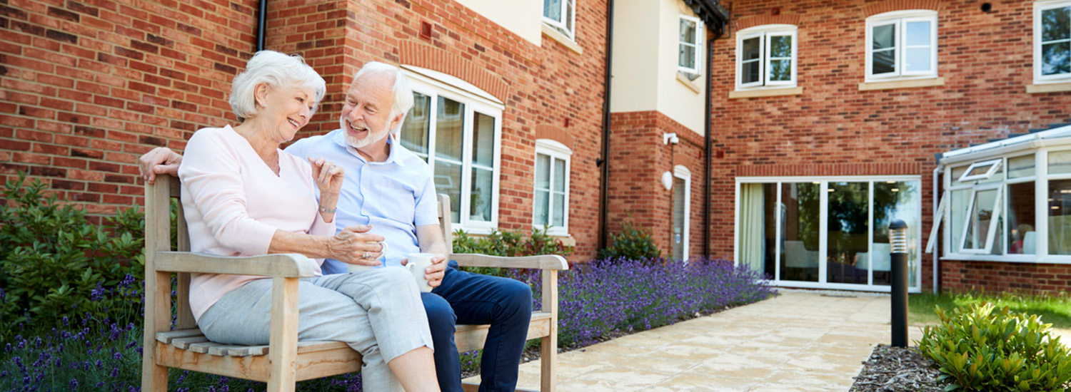 Senior couple laughing on bench in courtyard